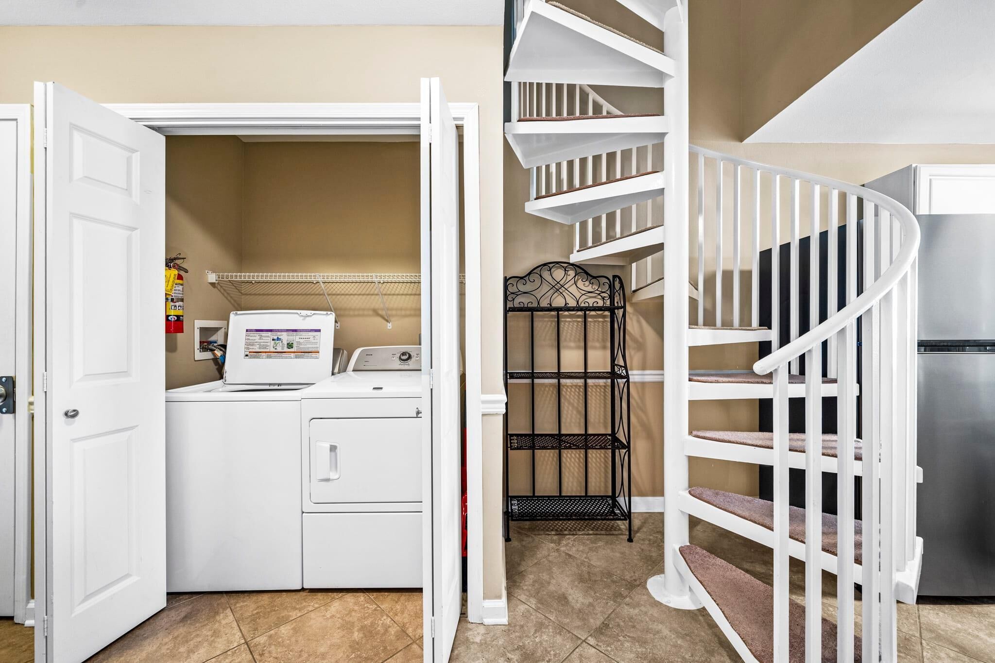 A laundry room with a washer and dryer, a metal rack, and a white spiral staircase.
