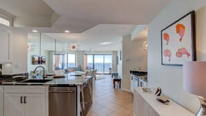 A modern kitchen with a central island, a dining area with a view, and a living space with a balcony. - Seachase 803w (Orange Beach)