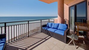 A balcony with a wicker sofa and a table, overlooking a beach. - Seachase 803w (Orange Beach)