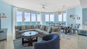 A spacious living room with a large sofa, a round coffee table, and a dining area with a table and chairs. - Lighthouse 918 (Gulf Shores)