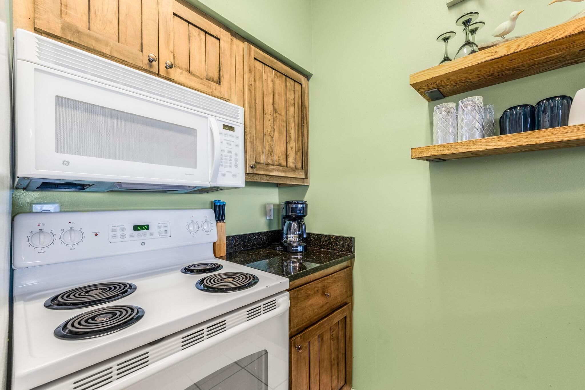 A kitchen with a white stove, a microwave, wooden cabinets, and a coffee maker on the countertop.