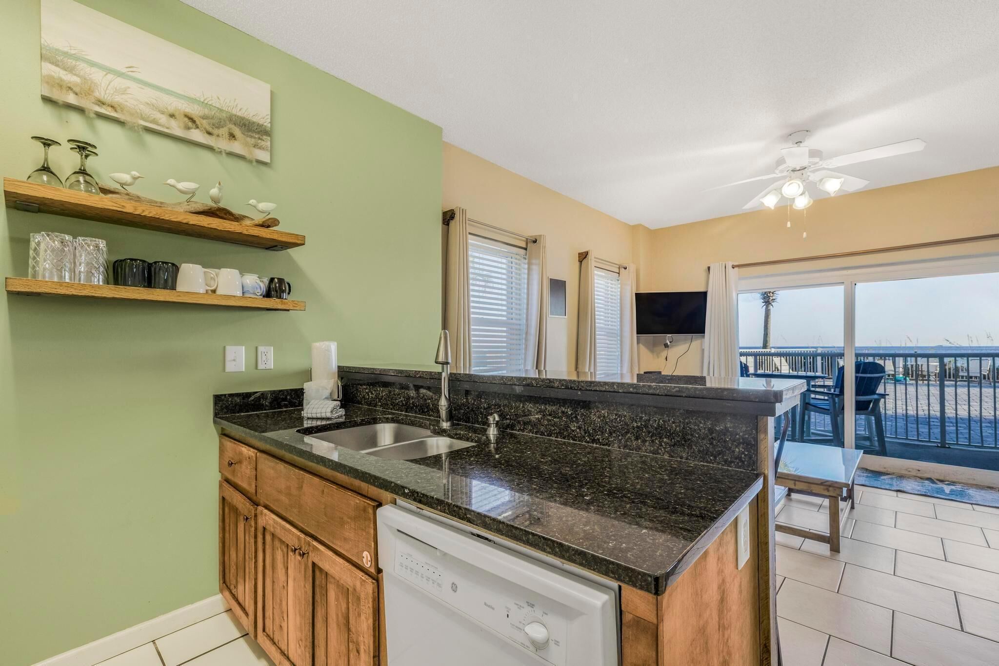 A kitchen with a granite countertop, wooden cabinets, a dishwasher, and a view to a balcony with outdoor seating.