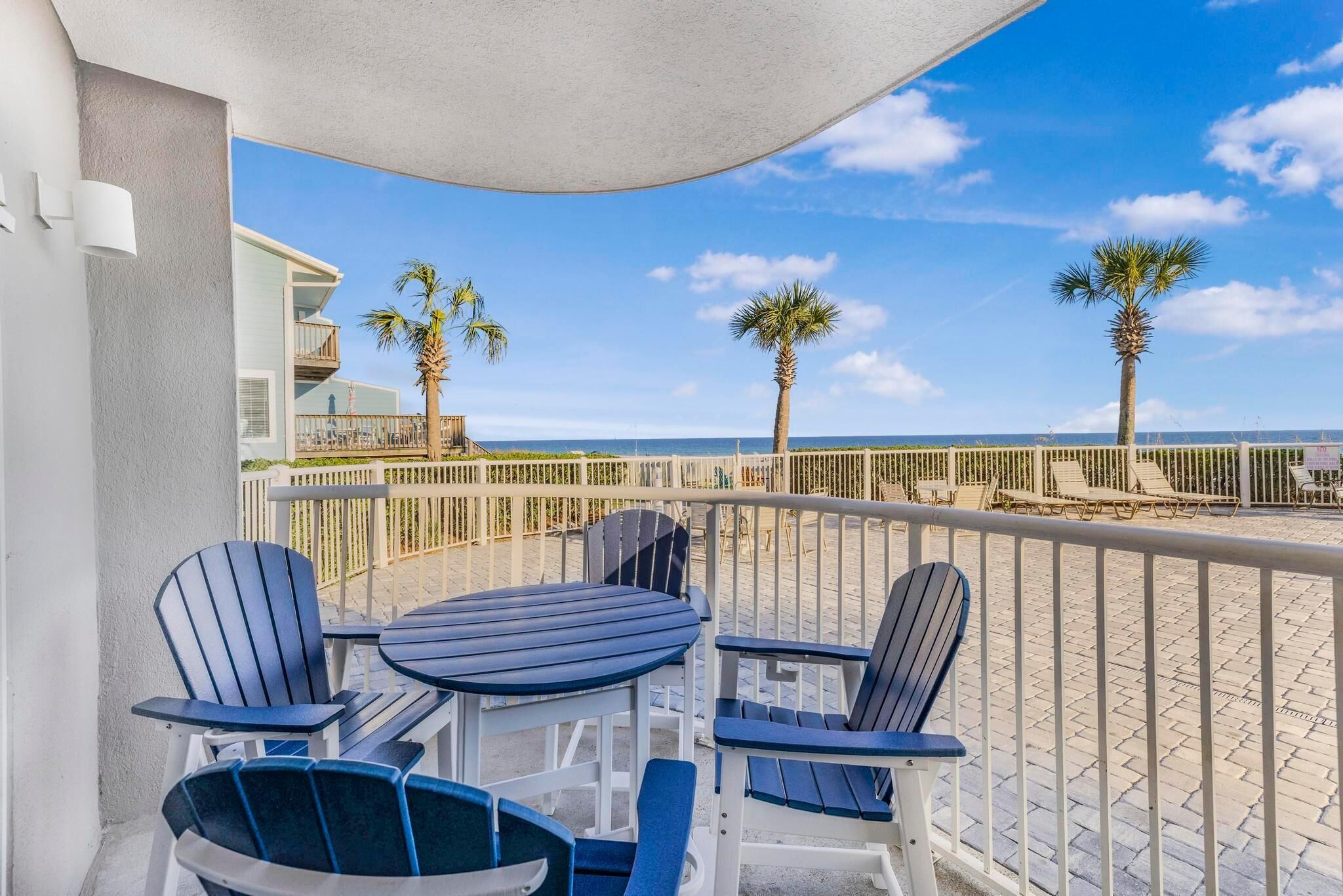A balcony with outdoor seating, palm trees, and a view of the beach.