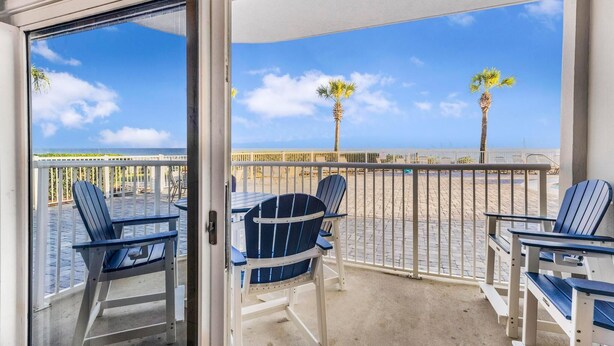A balcony with two Adirondack chairs, a table, and a view of the beach and ocean. - Tradewinds 001 (Orange Beach)