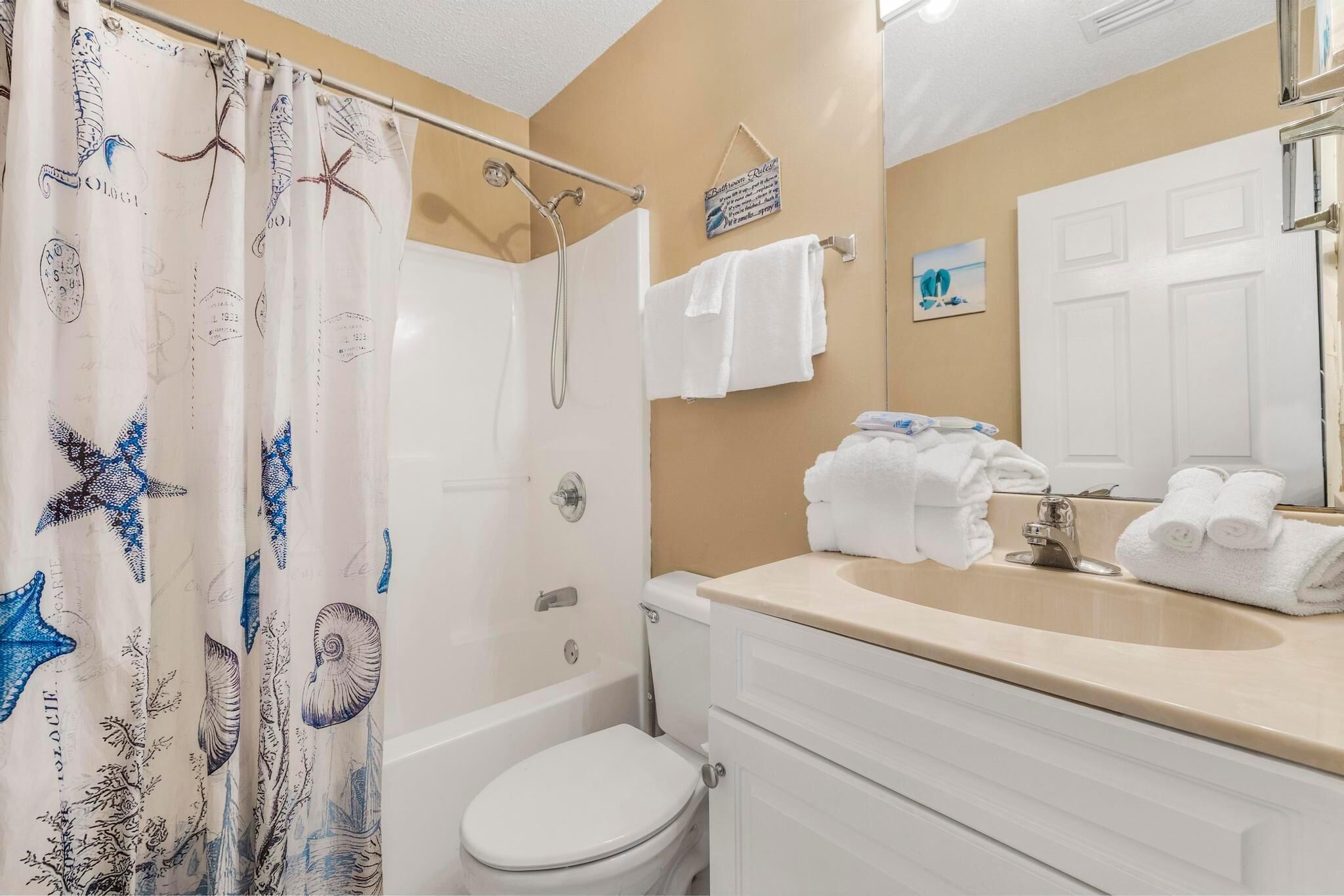 Een badkamer met een douchegordijn waarop zeedieren staan afgebeeld, een wit toilet, een wastafel met een beige blad en een spiegel boven de wastafel.