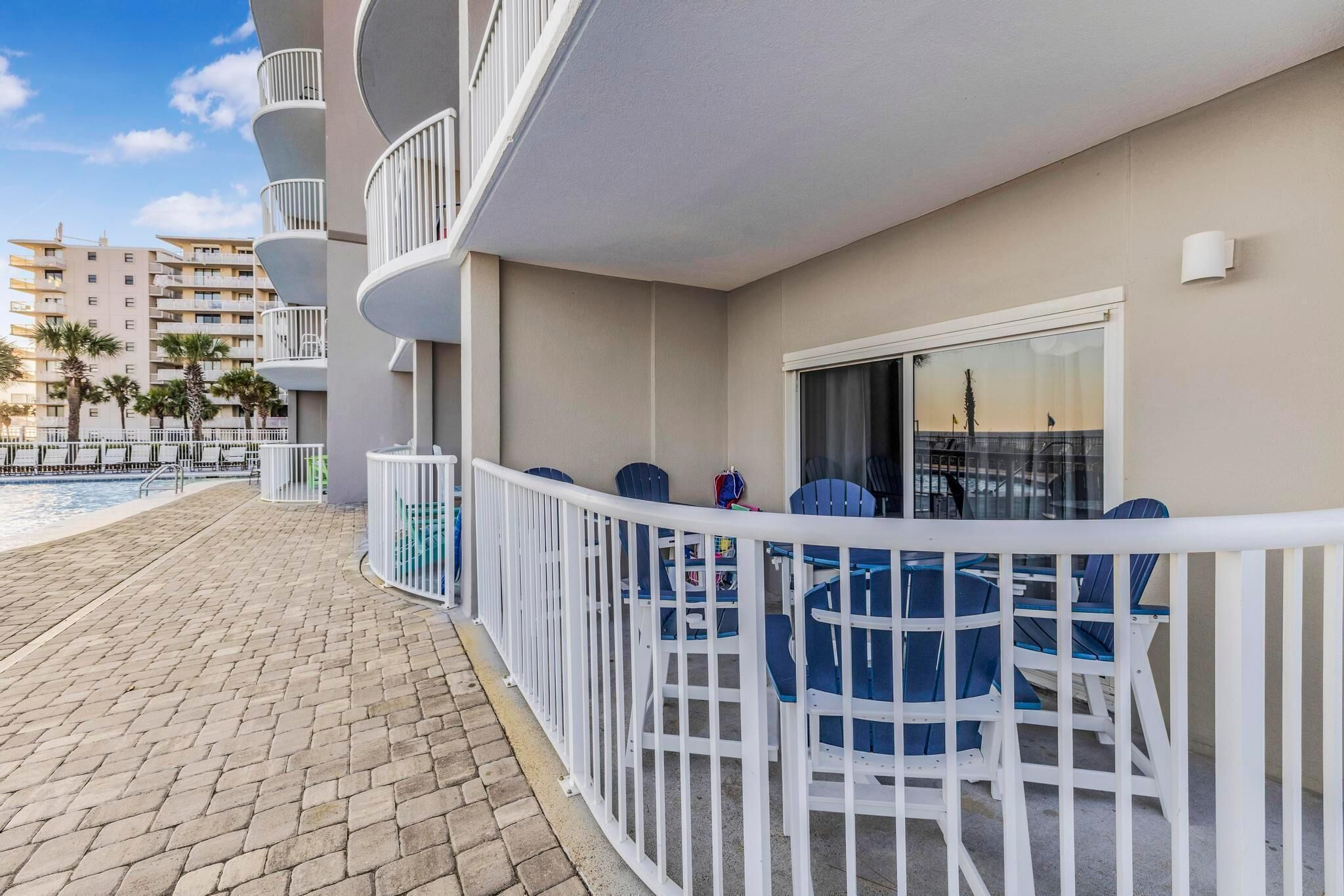 A balcony with blue chairs and a poolside area.