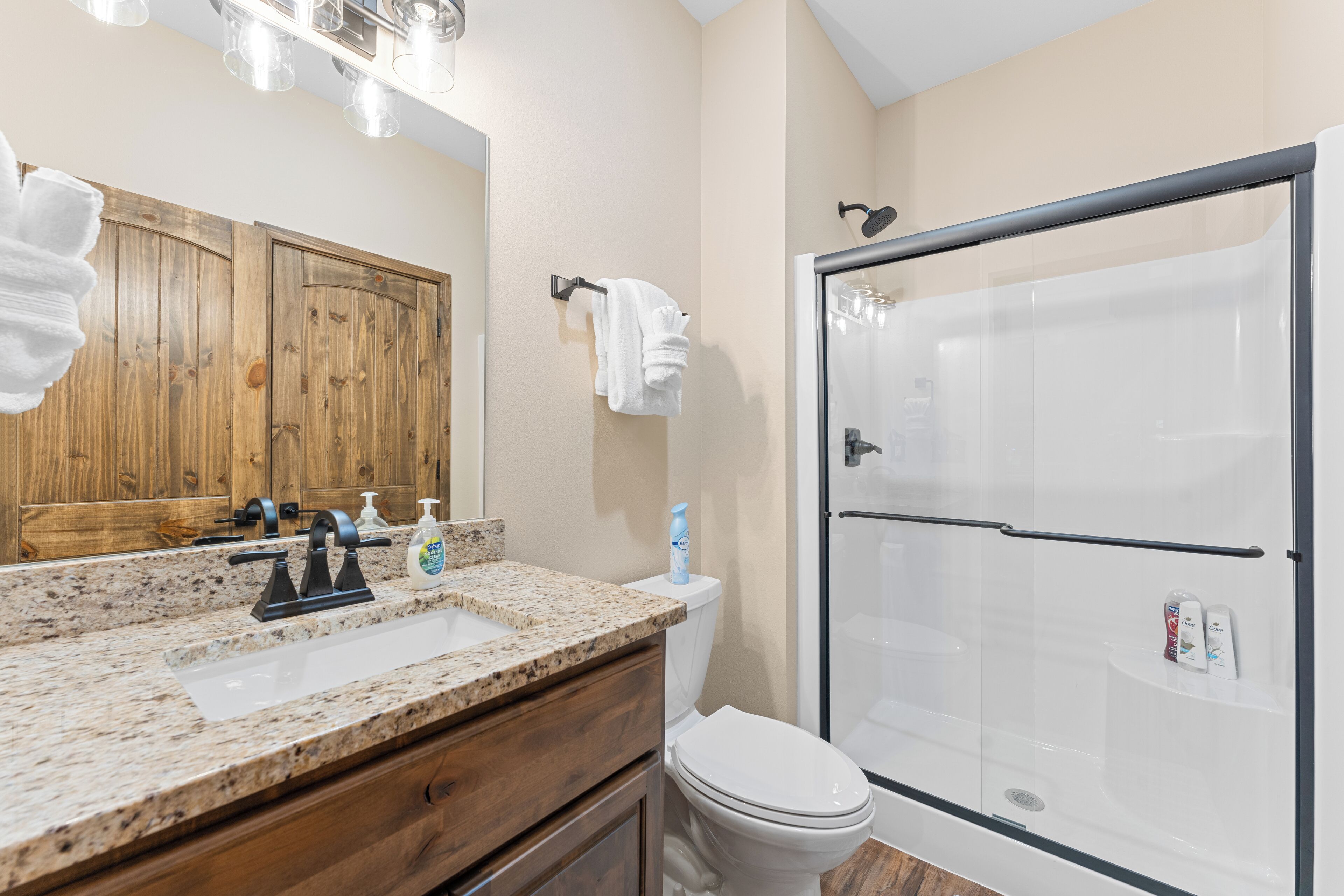 Une salle de bain dotée d’un comptoir en granit, de meubles en bois, de toilettes blanches et d’une douche à parois de verre.