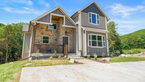 A two-story house with a stone facade, a large front window, and a well-maintained lawn.