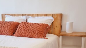 Une chambre à coucher bien rangée, avec une tête de lit en bois, un couvre-lit blanc et un plaid marron. Un tableau abstrait encadré est accroché au mur au-dessus du lit.