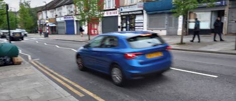 Cena de rua com um carro azul seguindo pela estrada.