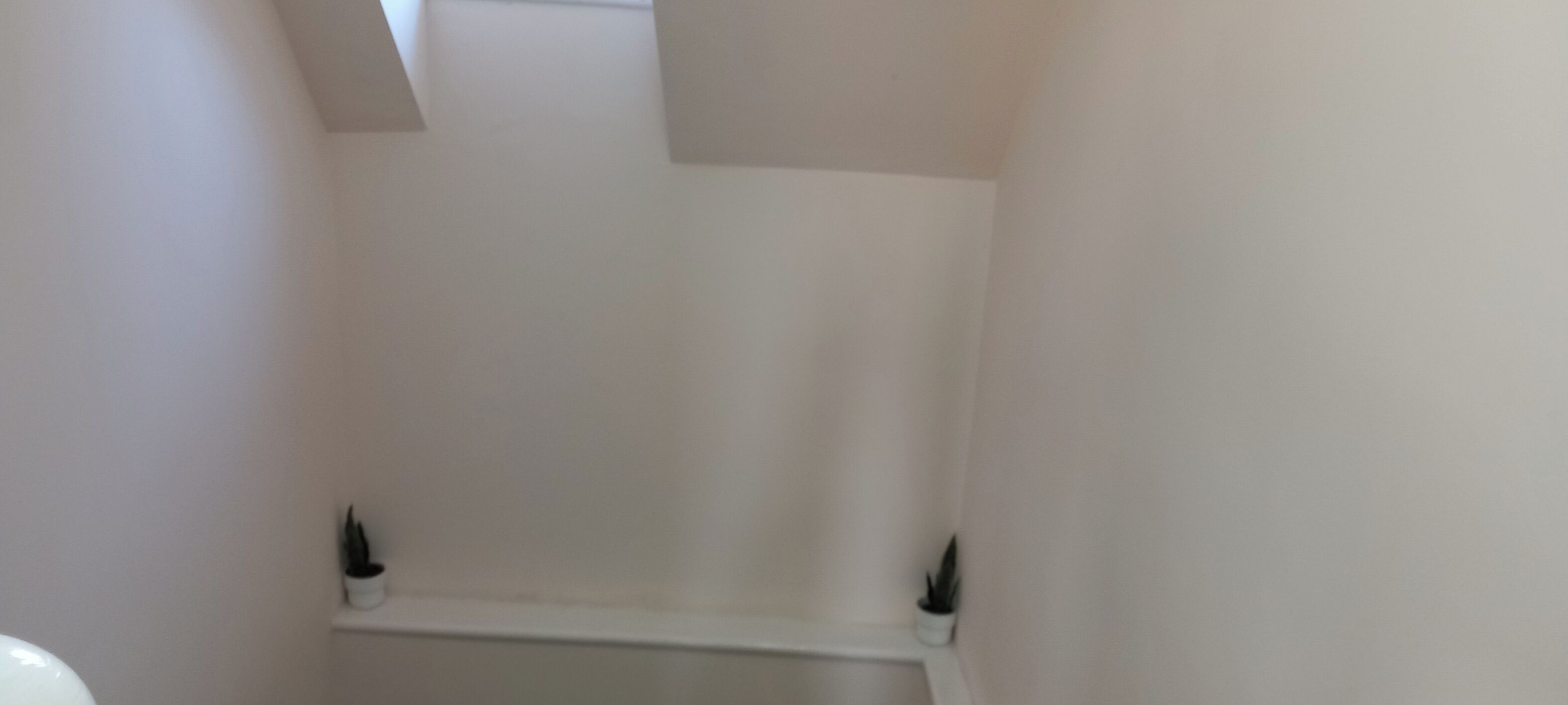 A narrow, white-walled bathroom with a small shelf at the bottom.