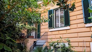 A residential building with a garden area, including a staircase leading to an upper floor, surrounded by lush greenery and potted plants. - Beautiful 2-bed Apartment in Roma (Rome)
