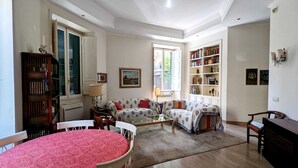 A living room with a round table, two sofas, a bookshelf, and a window. - Beautiful 2-bed Apartment in Roma (Rome)