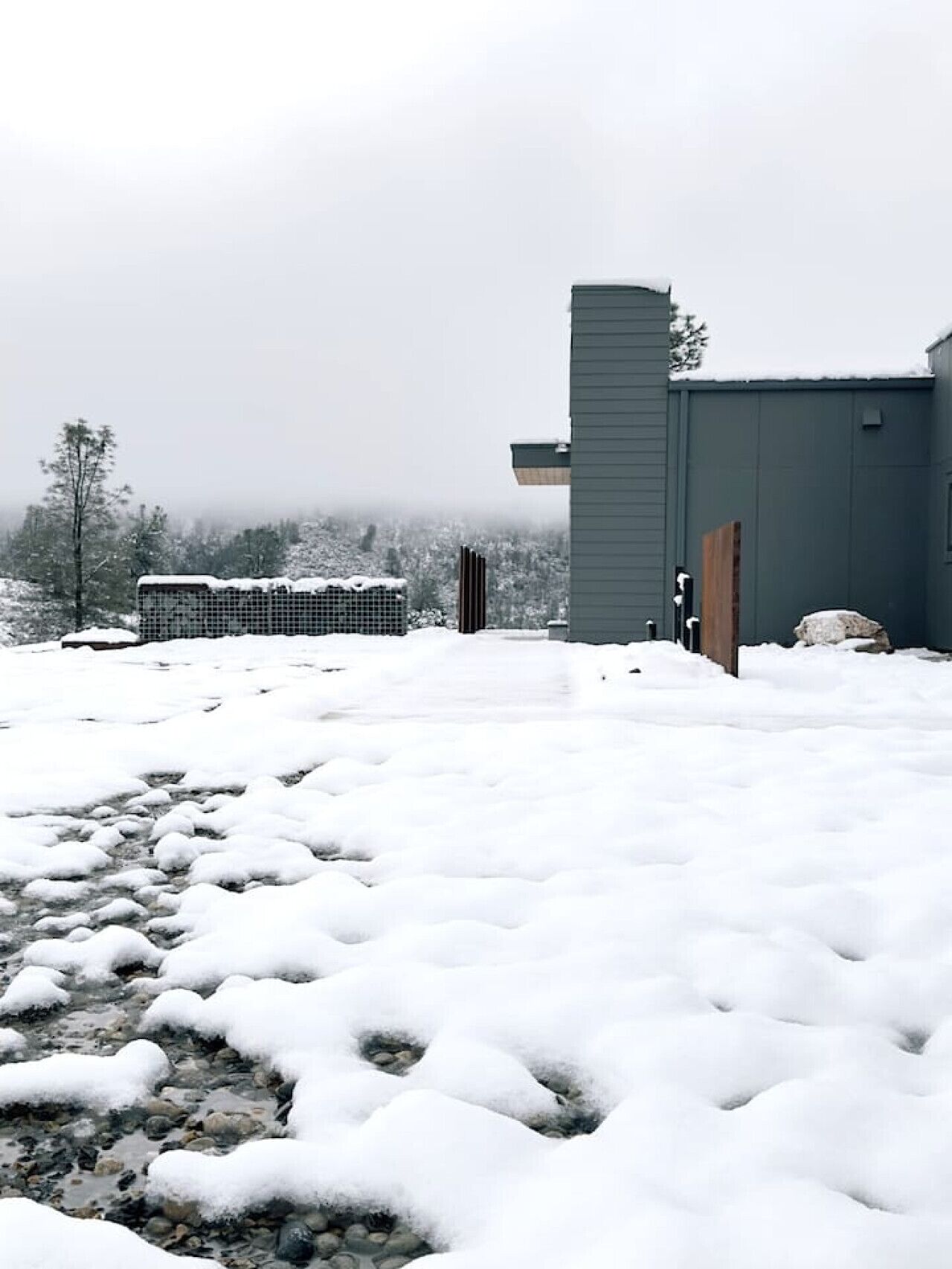 Paisaje nevado con un edificio de diseño moderno, un camino y una vista distante de árboles.