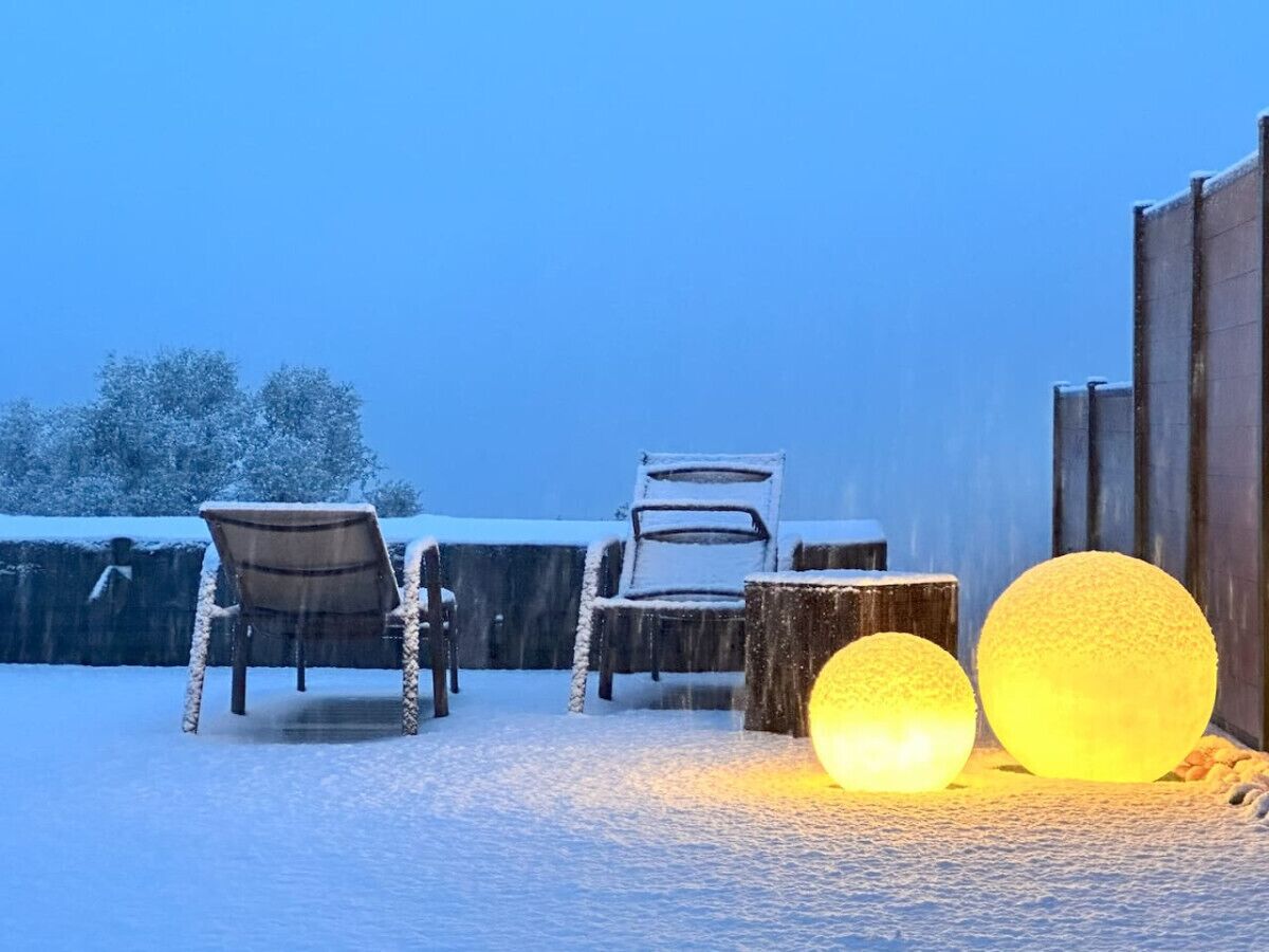 A snow-covered outdoor area with two chairs and a table, and two illuminated spherical objects.