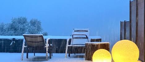 A snow-covered outdoor area with two chairs and a table, and two illuminated spherical objects.