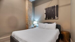 Een net opgemaakt bed met witte lakens in een kamer met een gestructureerde muur en een modern abstract schilderij.