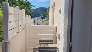 Een smalle buitenpassage met een metalen bankje en een poort die uitkomt op een prachtig uitzicht op een strand en bergen.