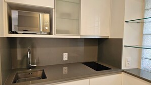 Een keuken met een ingebouwde magnetron, een RVS-gootsteen en een glazen plank.