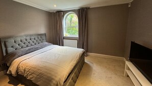 A bedroom with a large bed, a television, and a window with curtains. - Luxury Apartment In London - Pool Spa & Gym (London)