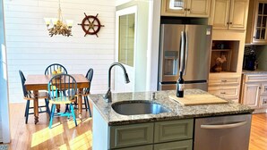 A kitchen with a granite countertop, a stainless steel refrigerator, and a dishwasher. There is a dining area with a wooden table and chairs. - Ocean view, private 4 Bedroom home just steps to the beach! (Old Orchard Beach)