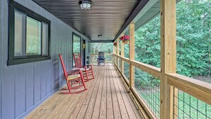 A covered porch with wooden railings, rocking chairs, and hanging flower baskets. - Cozy 3BR Getaway, Lake access, Fire Pit, Trails (Mount Airy)