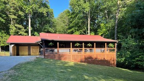 A two-story wooden cabin with a red roof, surrounded by a well-maintained lawn and dense forest. - Cozy 3BR Getaway, Lake access, Fire Pit, Trails (Mount Airy)
