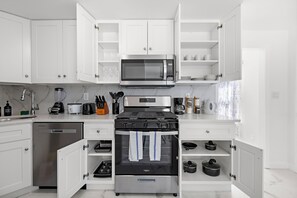 Una cocina moderna con armarios blancos, microondas integrado, estufa de acero inoxidable y lavavajillas.