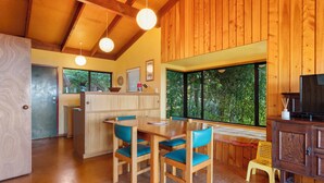 Un interior de madera con comedor, cocina y un amplio ventanal con vistas a la vegetación.