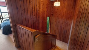 Un interior de madera con una escalera, un ventanal y una lámpara colgante.