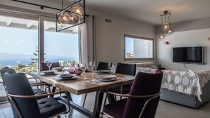 A dining area with a table set for four, chairs, and a view of the sea. - Modern Cycladic House (Naxos)