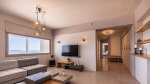 A modern living room with a sofa, coffee table, TV, and pendant lights. - Modern Cycladic House (Naxos)