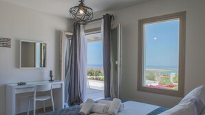 A bedroom with a bed, a desk, a chair, and a view of the sea through a window. - Modern Cycladic House (Naxos)