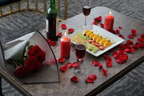 A table set with a wine bottle, glasses, a fruit platter, and rose petals.