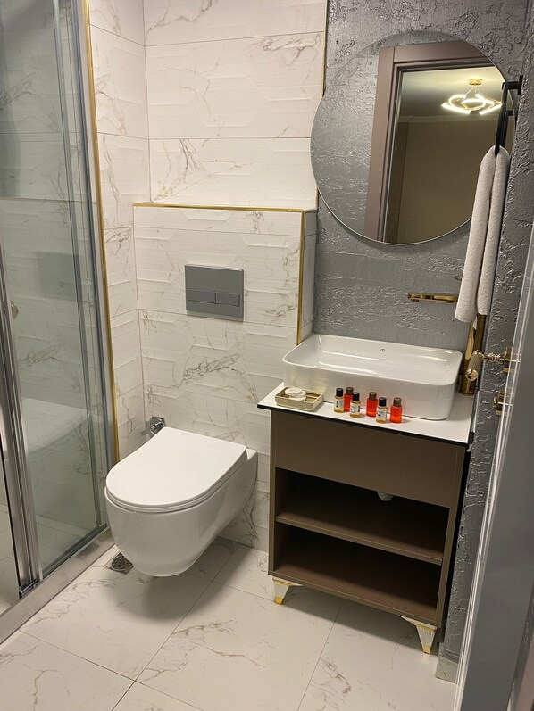 Un baño moderno con cabina de ducha de vidrio, inodoro blanco, tocador con lavabo y espejo.