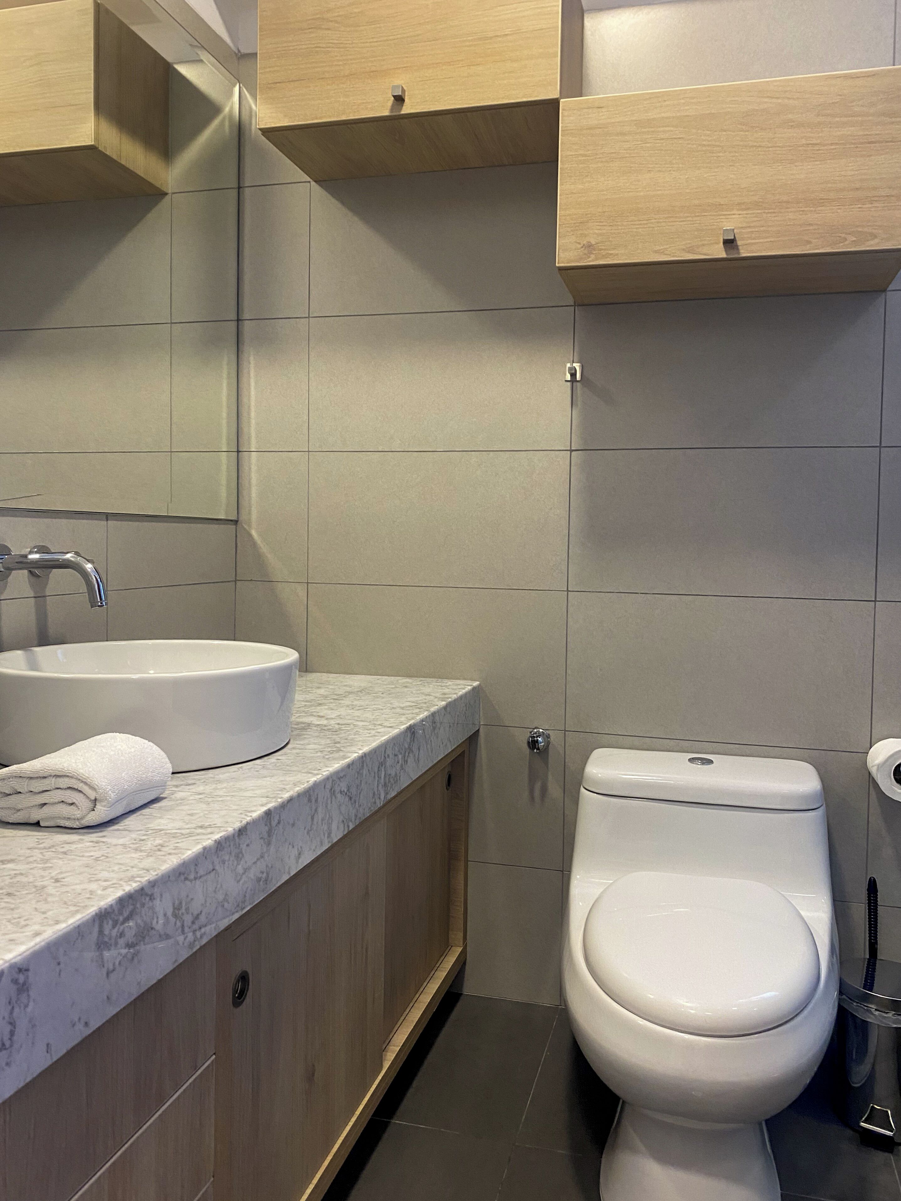 A modern bathroom with a marble countertop, a white sink, a toilet, and wooden cabinets.