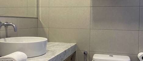 A modern bathroom with a marble countertop, a white sink, a toilet, and wooden cabinets.