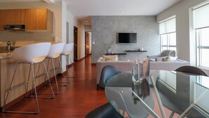 Una cocina moderna con armarios de madera, un comedor con mesa de vidrio y una sala de estar con sofá y televisor.
