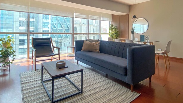 Una sala de estar moderna con sofá, sillones, una mesa de centro y grandes ventanales con vista a la ciudad.
