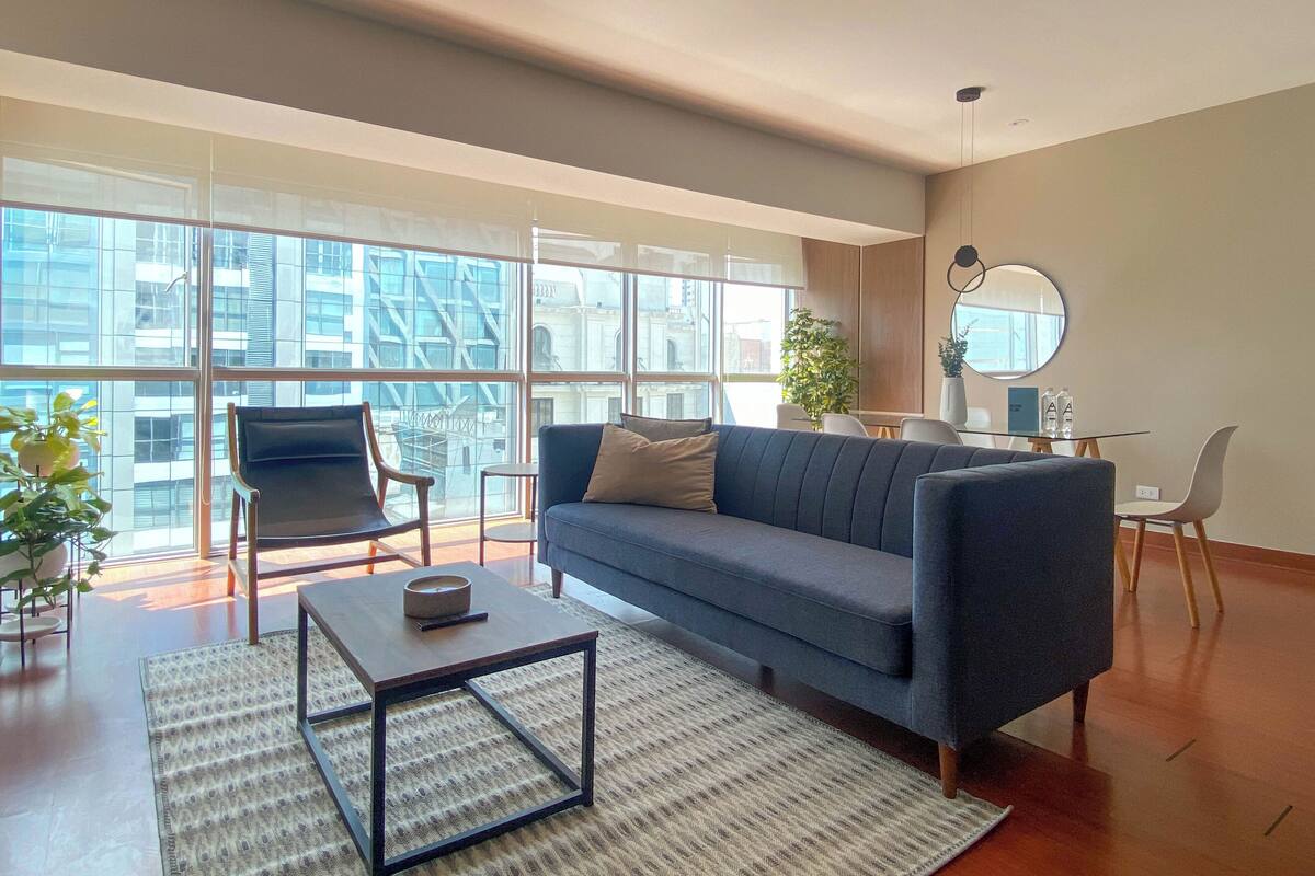 Ein modernes Wohnzimmer mit einer Couch, Sesseln, einem Couchtisch und großen Fenstern mit Blick auf die Stadt.