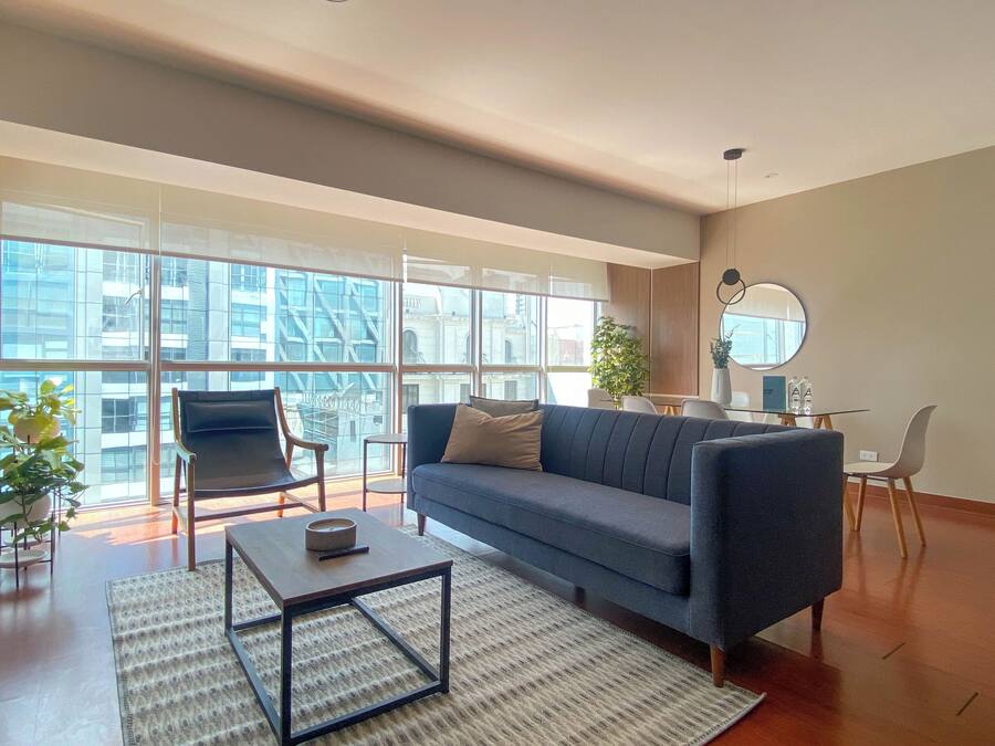 Una sala de estar moderna con sofá, sillones, una mesa de centro y grandes ventanales con vista a la ciudad.