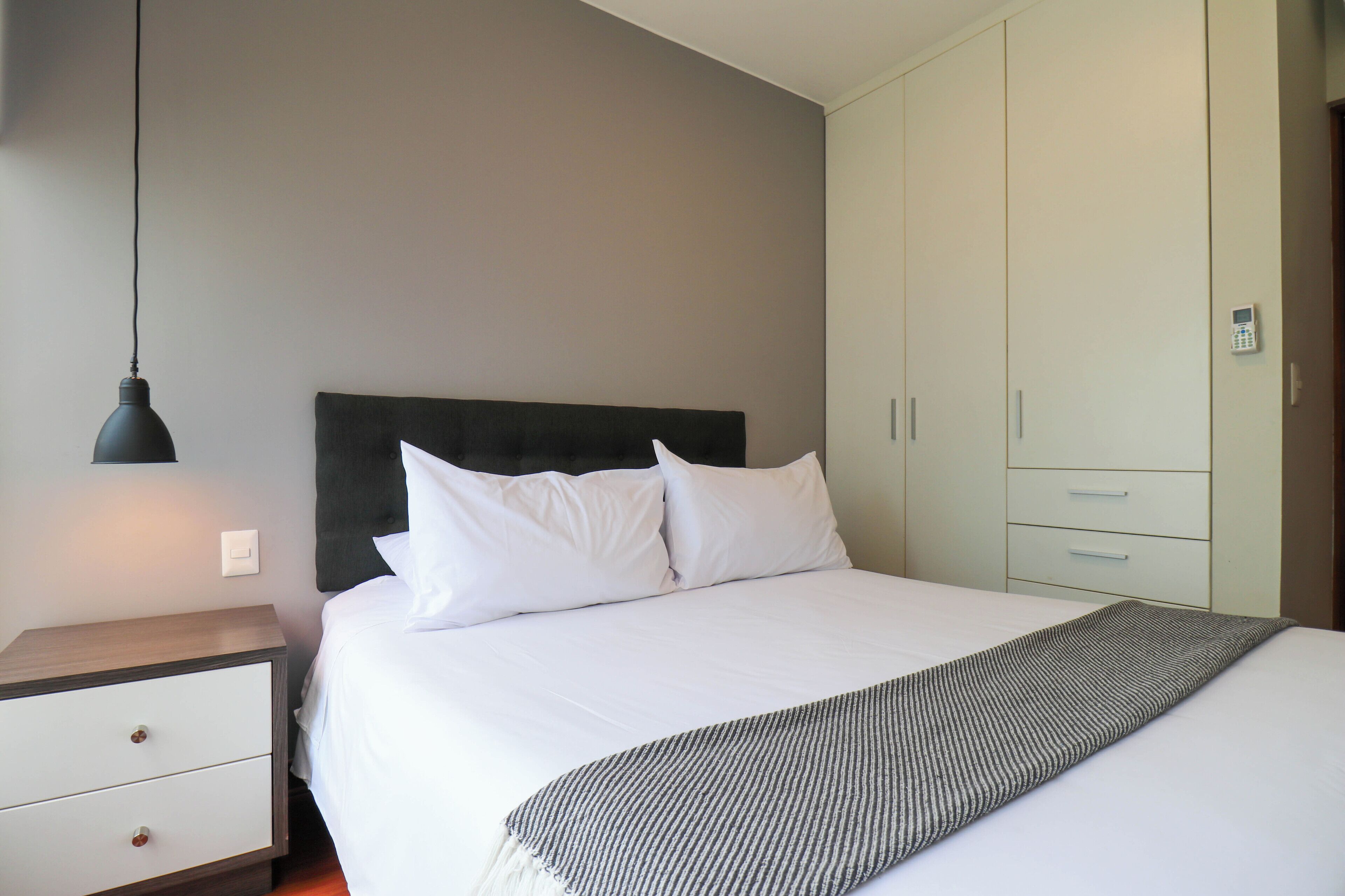 A bedroom with a bed, bedside table, lamp, and wardrobe.