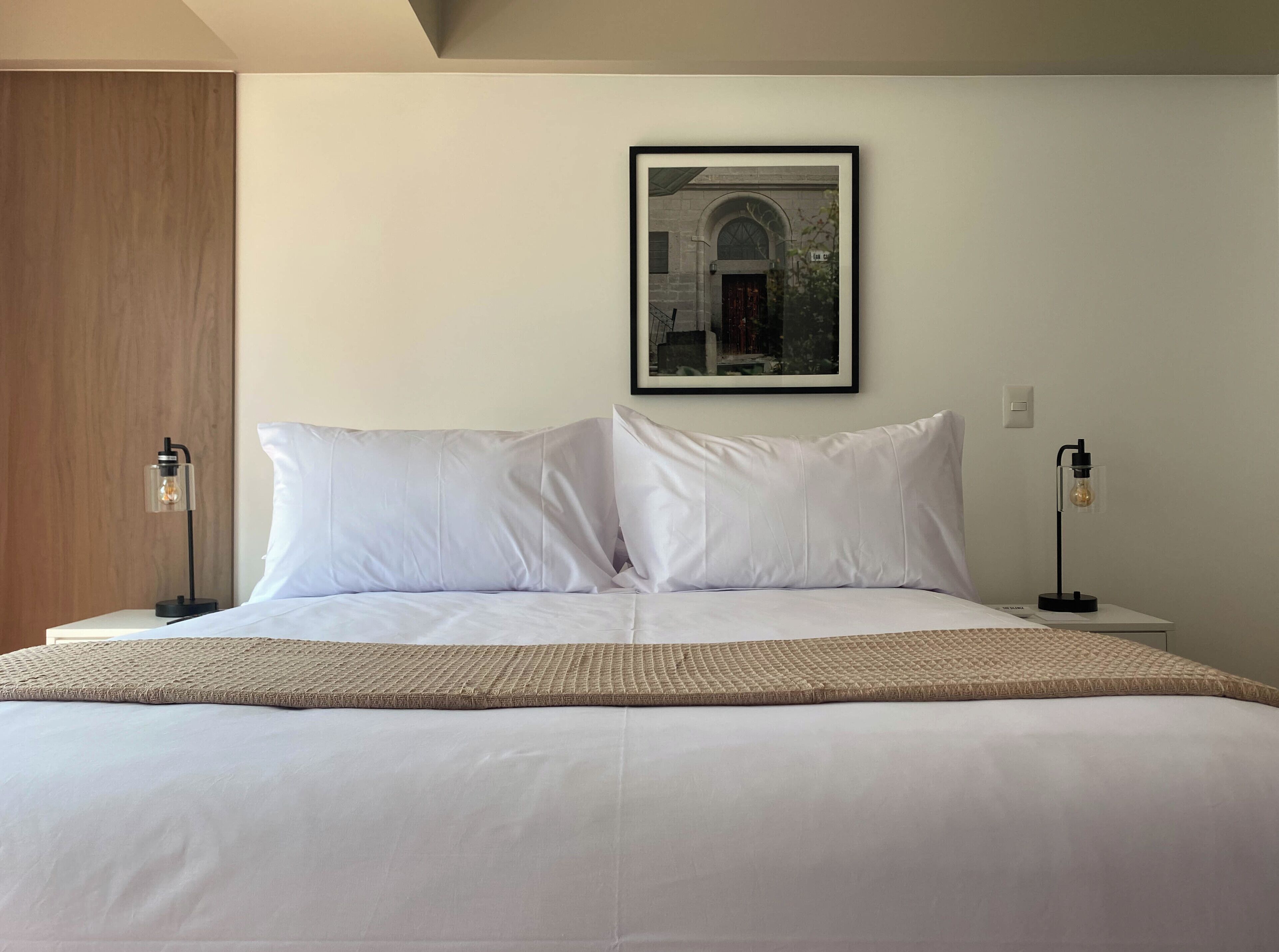 A neatly made bed with white linens, two bedside lamps, and a framed picture on the wall.
