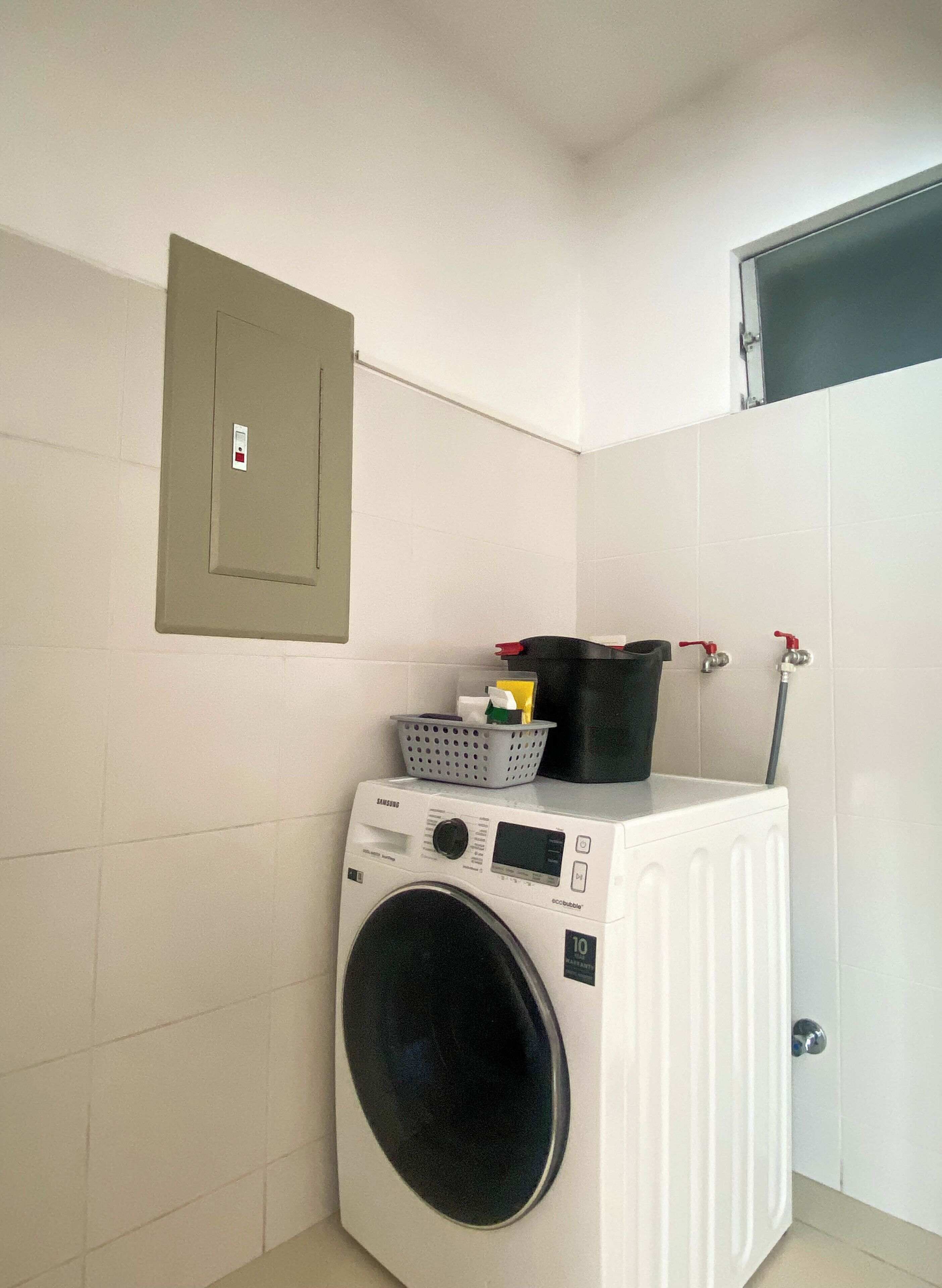 A compact laundry room with a front-loading washing machine, a utility box, and a water heater.