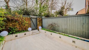A modern outdoor patio with a concrete floor, a wooden fence, and a stone wall. - The Nothinghill Charmer (London)