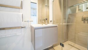 A modern bathroom with a glass shower enclosure, a white vanity with a gold towel rack, and a large mirror above the sink. - The Nothinghill Charmer (London)