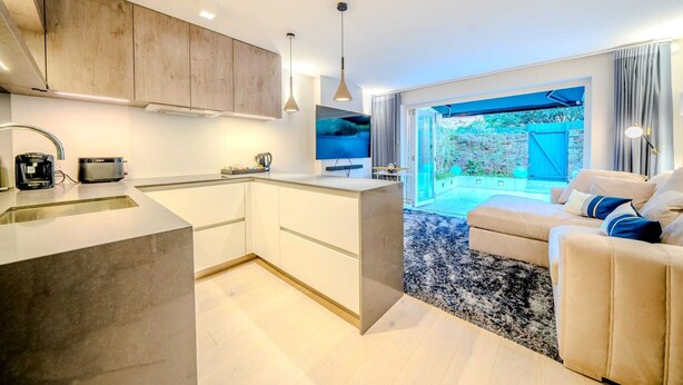 A modern kitchen with a central island, a dining area with a sofa, and a view of a pool. - The Nothinghill Charmer (London)