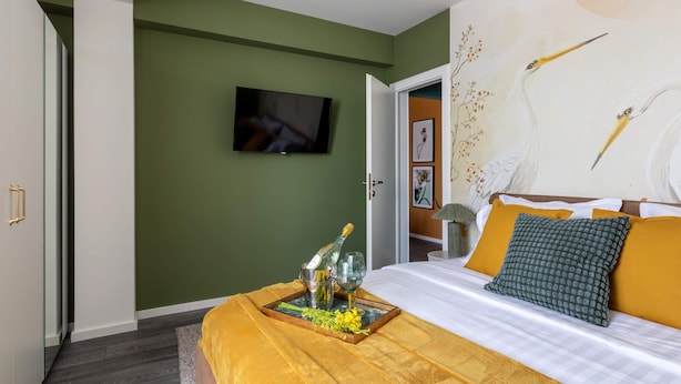 A hotel room with a bed, a television on the wall, and a tray with champagne and flowers. - Lucky Cranes (Bucharest)