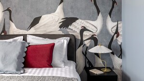 A bedroom with a bed, pillows, a nightstand, a lamp, and a wall mural of birds. - Lucky Cranes (Bucharest)