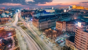 A cityscape at dusk with illuminated buildings, a busy intersection, and a prominent roundabout. - Lucky Cranes (Bucharest)